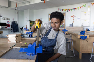 African American boy learning carpentry in woodworking class at school
