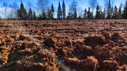 Freshly plowed brown soil stretches into the distance beneath a bright blue sky adorned with fluffy...