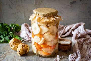 Pickled vegetables in a glass jar on a gray background. Jerusalem artichoke pickled in a jar. Close-up.