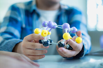 Student is studying simulate shape of covalent molecules by connecting molecular function shapes on the desk in Chemistry lesson, soft focus.