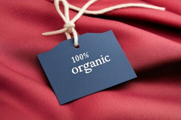 Minimalist elegant 100% organic tag on dark red fabric background