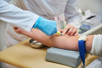 A woman is drawing blood from a man's arm. The woman is wearing gloves