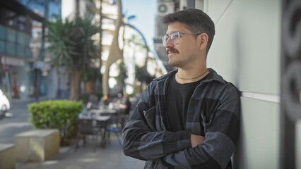 Handsome young hispanic man with moustache standing arms crossed on a sunny city street