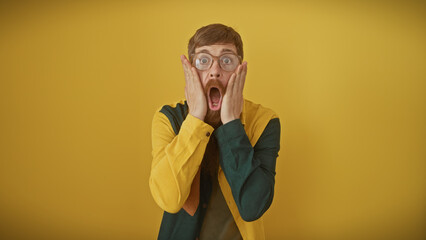 Shocked redhead man with beard and glasses against yellow background showing surprise expression,...