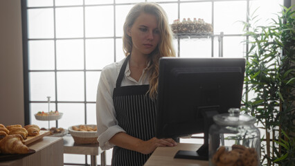 Young woman working as a baker in a bakery shop, wearing an apron and standing behind a counter...