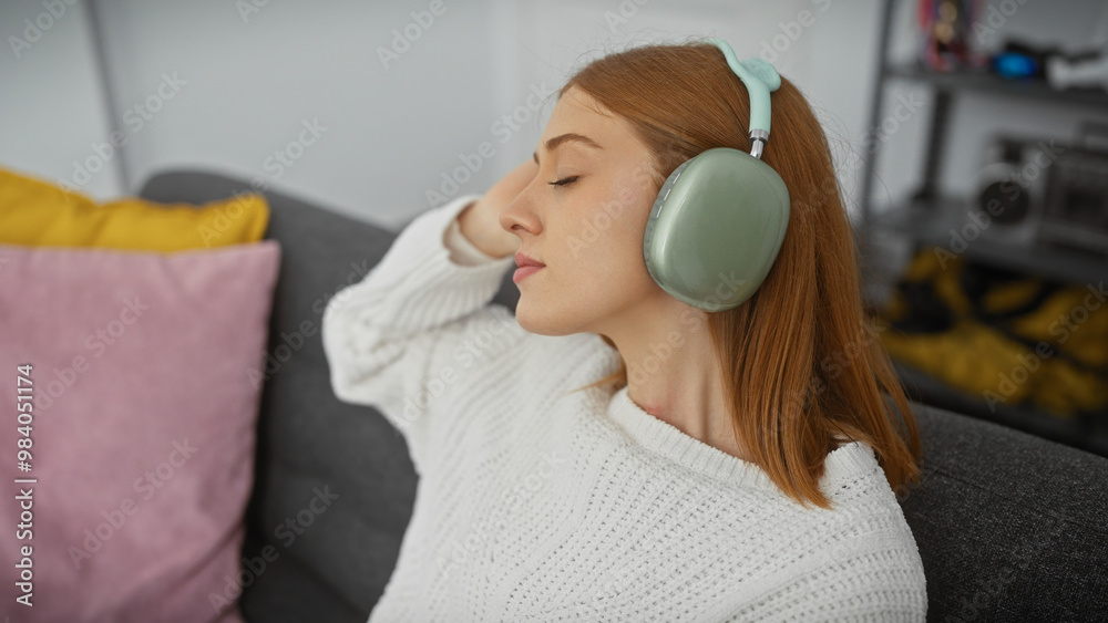 Sticker A serene young woman enjoys music with headphones, relaxing on a sofa in a cozy living room setting.