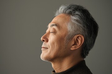 Fototapeta premium Photo of a mature, handsome Japanese man with gray hair, eyes closed in profile view on a gray background, with side lighting.generated ai