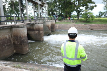 Portrait of engineer wearing green vest and white helmet with tablet Working day on a water dam with a hydroelectric power plant. Renewable energy systems, Sustainable energy concept