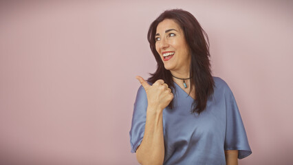 Fototapeta premium Mature hispanic woman pointing sideways, smiling, isolated on a pink background.