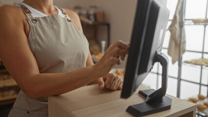 Hispanic woman working in a bakery and using a touchscreen register while dressed in an apron...