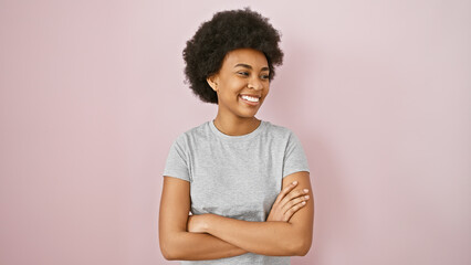 Fototapeta premium Confident african american woman with curly hair smiling against a pink wall isolated background