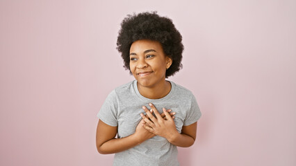 African american woman with curly hair smiling, hand on chest, against a pink background, evoking...