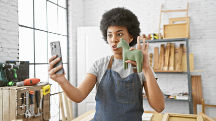 African american woman with curly hair takes selfie with ceramic horse in a carpentry workshop
