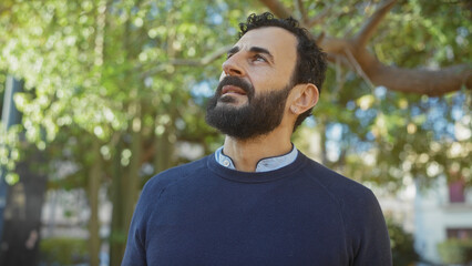 Middle-aged bearded man in contemplation amidst green park foliage, exuding serenity and introspection.