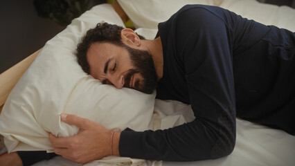 Obraz premium A bearded middle-aged man in a black shirt rests peacefully on a white pillow in a bedroom setting, exuding tranquility and relaxation.