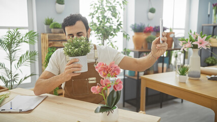 Smiling man with beard smells flowers at a florist shop while holding a phone for a selfie.