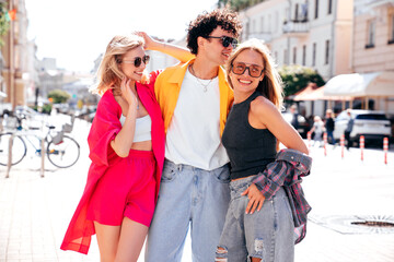 Group of young three stylish friends posing in the street. Fashion man and two cute female dressed in casual summer clothes. Smiling models having fun. Cheerful women and guy outdoors, sunglasses