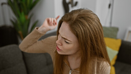 Fototapeta premium A contemplative young blonde woman in a casual sweater indoors, seated in a modern living room.