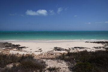 Scogliera rocciosa che si affaccia sul mare turchese, cielo blu senza nuvole e spiaggia bianca