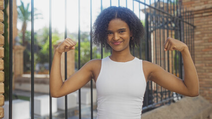 A beautiful young african american woman with curly hair confidently flexing her muscles in an...