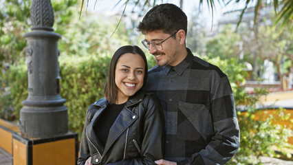 Fototapeta premium A loving couple embraces on a city street, surrounded by urban greenery and warm sunlight.