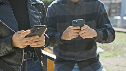 Close-up of a young couple engrossed in their smartphones on a sunny urban street.