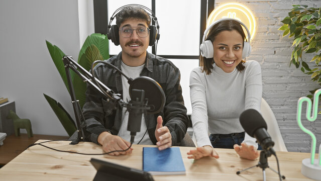 A man and woman smile as podcast hosts in a modern studio with microphones and headphones, symbolizing a casual broadcasting setup.