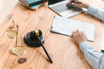 A person writes notes while using a laptop beside a gavel and scales of justice, symbolizing legal...