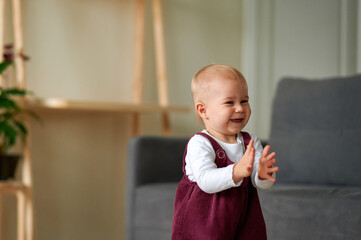 The adorable blonde-haired little girl smiles and claps her hands. The cute little girl is happy.