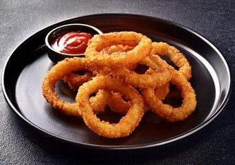 onion rings on a black plate with a small bowl of chili sauce
