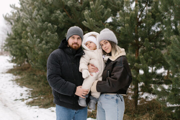 Parents and little child in a pine forest in winter. 