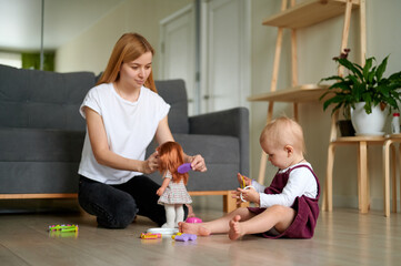 Mum and young daughter playing together on the floor. Mother and little girl playing hairdresser with plastic brightly coloured toys.
