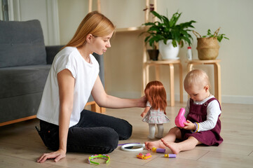 Fototapeta premium Young Caucasian mum playing with her cute little daughter on the floor. Mum and daughter playing in a hairdresser's shop.