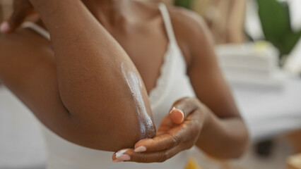 African american woman applying lotion to her elbow in a spa wellness center, highlighting a serene and relaxing beauty treatment setting with focus on skin care and self-care.