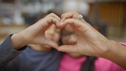 Fototapeta premium A woman and a boy make a heart shape with their hands outdoors, symbolizing familial love and bonding in nature.