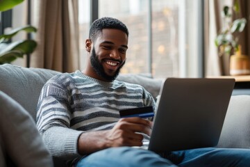 A man lounging comfortably in a modern living room, holding a credit card in one hand while
