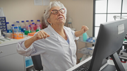 A senior woman scientist stretching in a laboratory, showing a moment of relaxation at work.