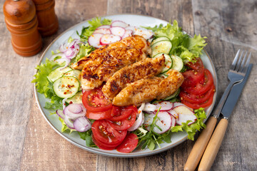 Warm salad with baked chicken breast and fresh vegetables, dressed with olive oil on a wooden background. Home kitchen in rustic style. Hearty delicious food. Selective focus, close-up.