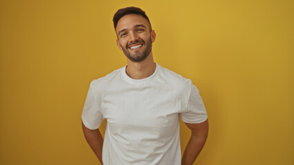 Handsome young hispanic man smiling confidently over an isolated yellow background, showcasing a...