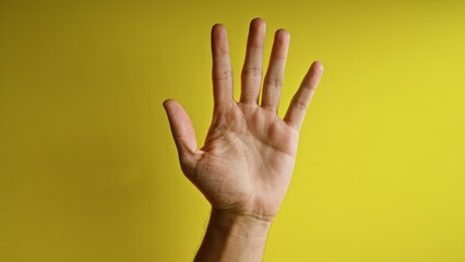 Hand raised against a vibrant yellow background, emphasizing fingers and palm details in a close-up composition