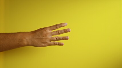 Man showing four fingers against a yellow background, highlighting an isolated close-up of a hand gesture with a solid vibrant backdrop