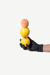 Hand with a black glove holds lemon and peach on bright background. Creative concept of clean healthy food