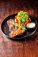 Grilled steak on a black plate with a side salad and sauce. Perfect for culinary, food photography, or restaurant menu content. High-quality image showcasing delicious, well-prepared cuisine.