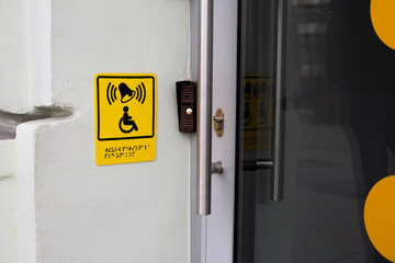 Sign with wheelchair and braille text at entrance to building near help button for people with disabilities, modern facilities for the disabled people