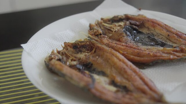 Fried Bangus on plate on top of bowl, with tissue paper under, orbit