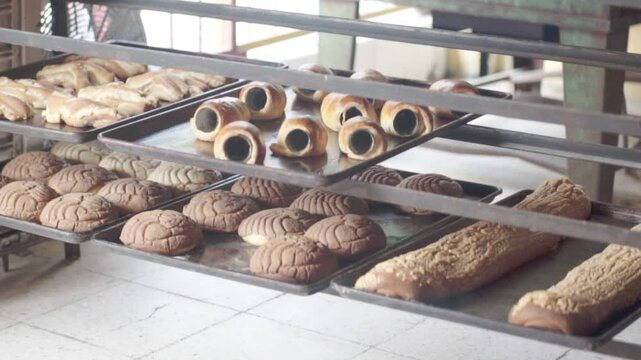 Close-up of multiple trays filled with assorted baked pastries cooling on racks inside a bakery.