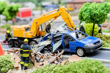 A diorama showing an emergency scene with firefighters responding to a car accident. A wrecked blue car is being recovered by a crane, surrounded by debris and rescue workers.