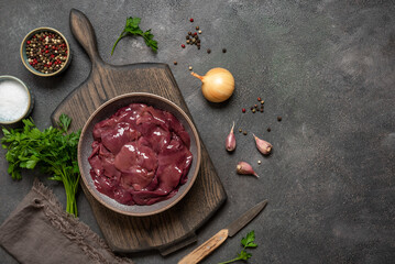 Fresh raw chicken liver with spices in a bowl on a dark grunge background. Place for your recipe. Top view, flat lay.