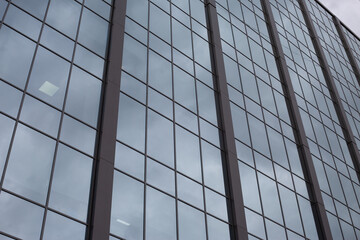 Fototapeta premium Glass facade of building goes up into the gray gloomy sky, cloudy sad day for routine work in office