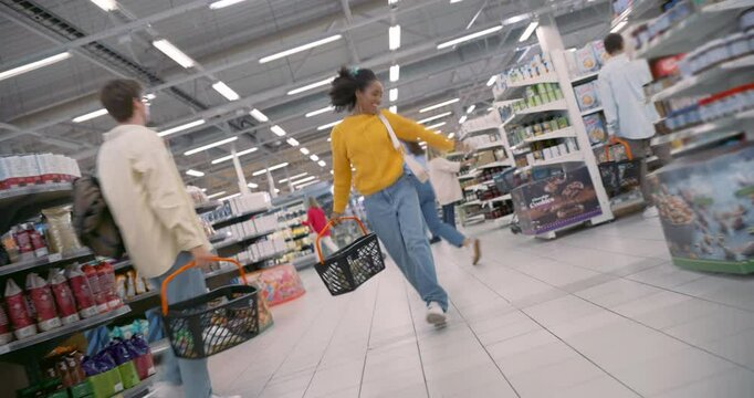 Cheerful Young African Female in a Yellow Sweater Performing a Dance in Modern Supermarket, Between the Stack Aisles with Food Produce. Diverse Customers Buying Groceries, Shopping 